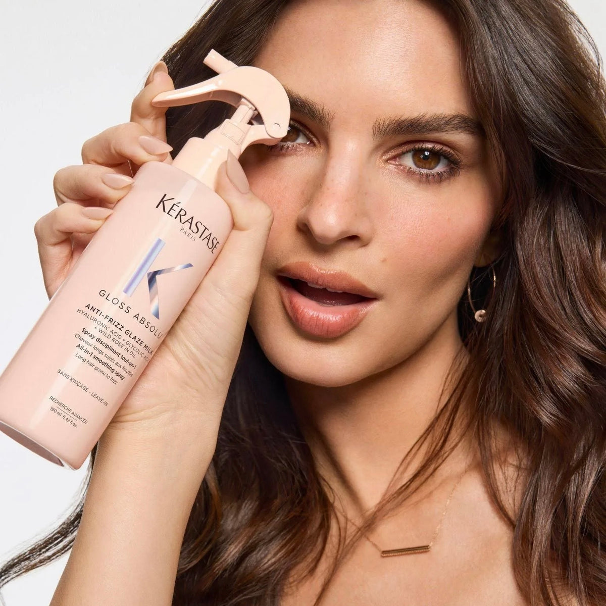 Kvinna håller Kérastase Gloss Absolu Anti-Frizz Glaze Milk leave-in-spray