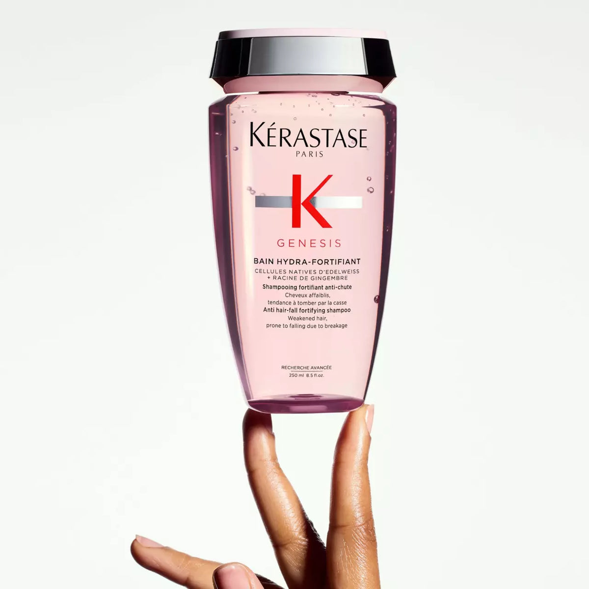 Kérastase Genesis Bain Hydra-Fortifiant Shampoo hålls i handen mot ljus bakgrund